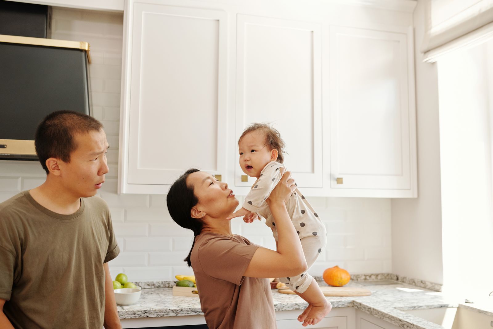 Parents lifting their baby together in the kitchen