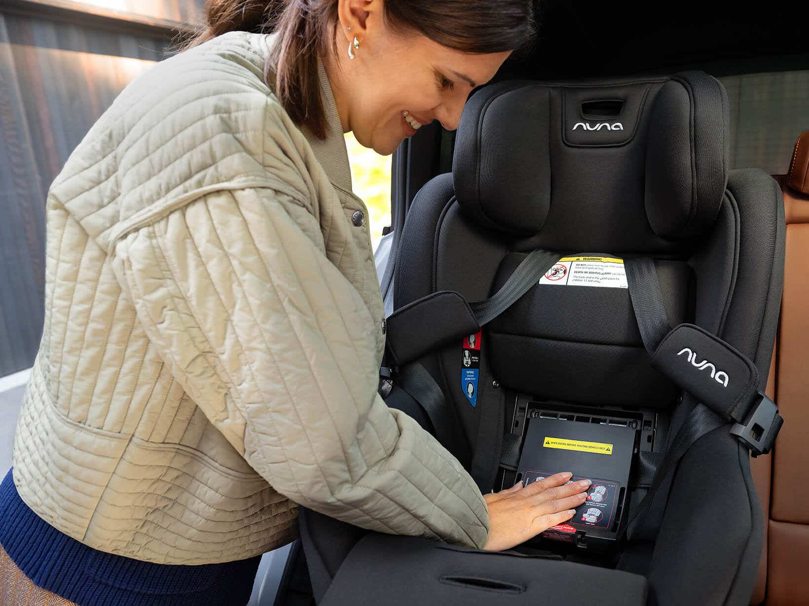 Parent installing the black Caviar Nuna RAVA next convertible car seat, hand on the base near the True Tension door