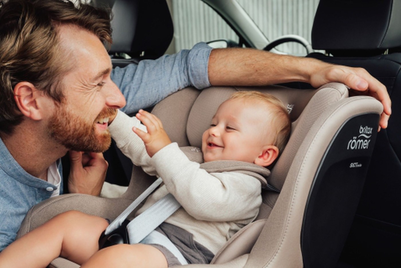 A father laughing with his baby secured in a Britax Römer 5-point-harness car seat